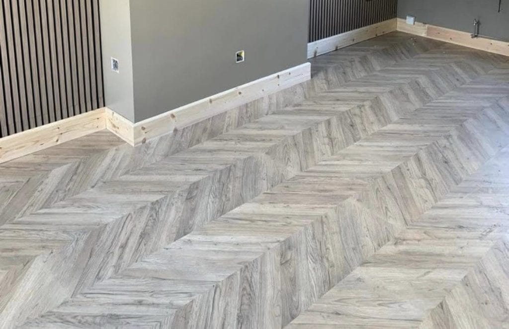 Grey wood-effect luxury vinyl tiles laid in herringbone pattern with white skirting