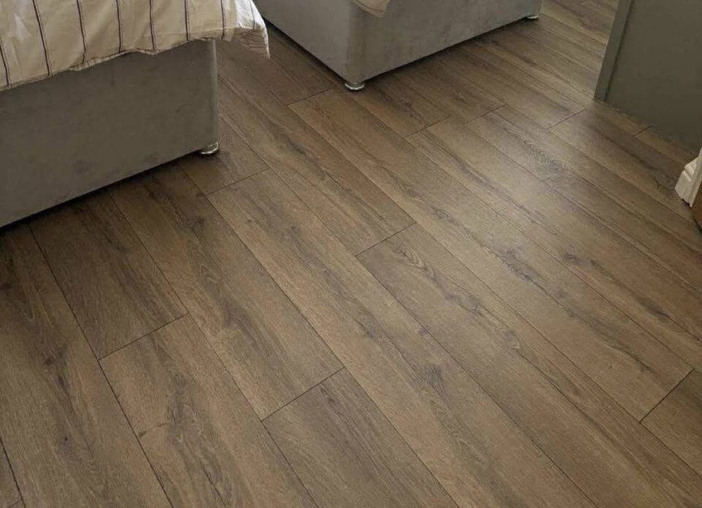 Warm brown wood-effect laminate flooring in a bedroom with grey upholstered bed