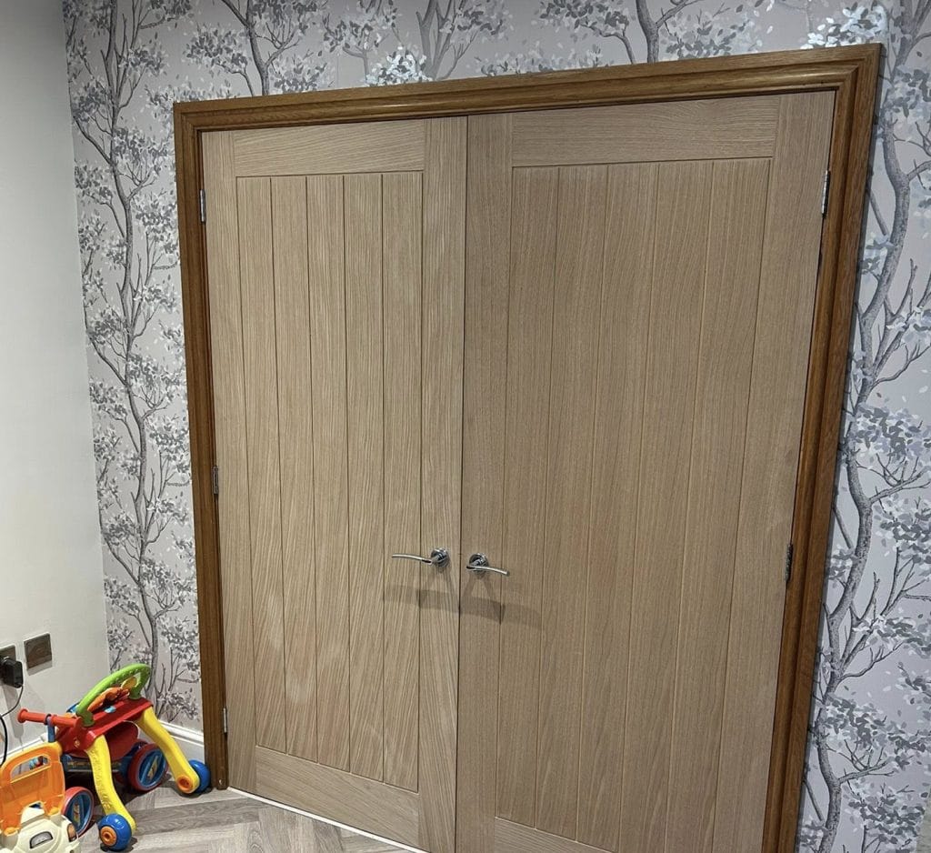 Oak double wardrobe doors with vertical grain panelling against decorative tree wallpaper
